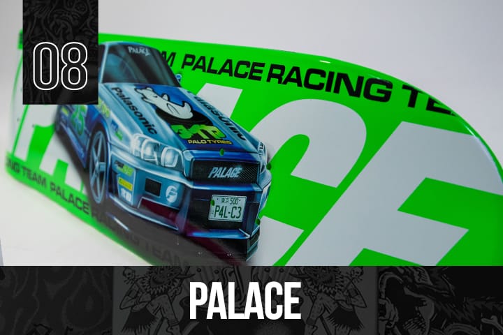Palace Skateboards deck with a green base and detailed blue racing car graphic, featuring Palace Racing Team branding, displayed on a white background.
