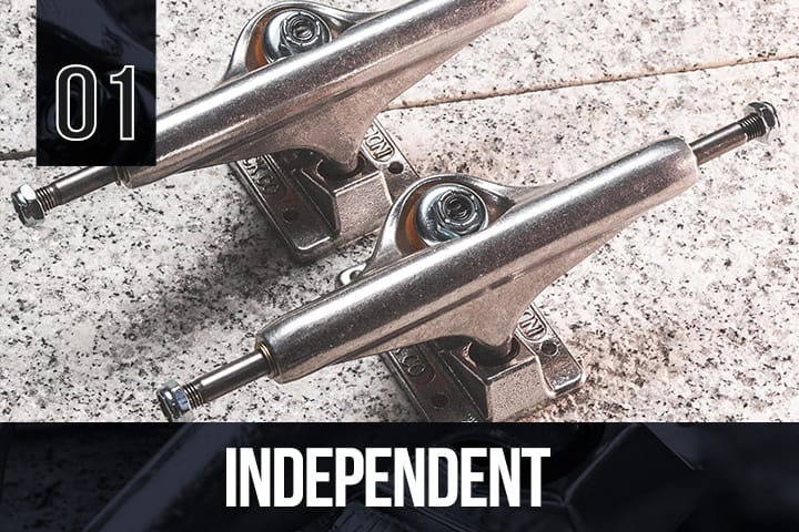 Two silver Independent skateboard trucks placed side by side on a light granite surface, highlighting their polished metal finish and sturdy construction.