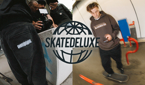 Streetwear scene with a focus on black jeans with eye-catching lettering and a brown hoodie with skatedeluxe print, skateboarder in a modern urban setting.