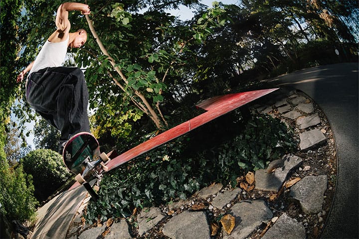 Andrew Verde macht einen switch fs crooked an einer Ledge im Park; Bäume und Weg bilden den Hintergrund.