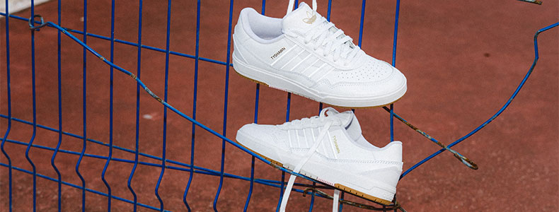 Top view of white adidas Tyshawn Jones signature sneakers with gold branding on a red textured surface.