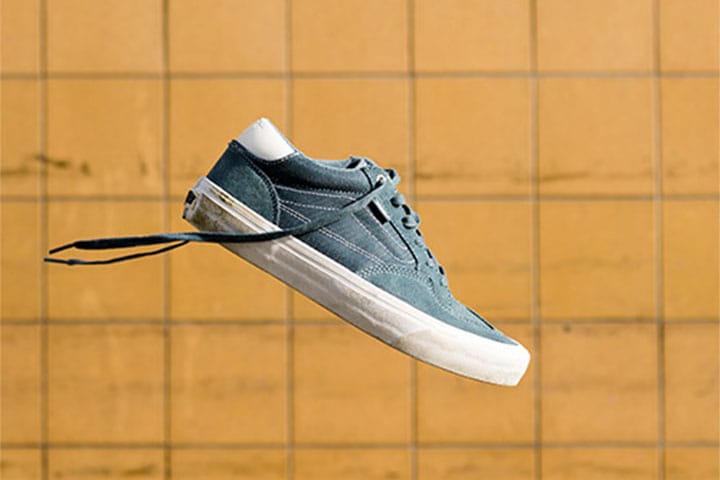 Primer plano lateral de unas zapatillas de skate Vans Rowan Pro de ante verde turquesa que parecen flotar delante de una pared de azulejos amarillos, con los cordones desatados.