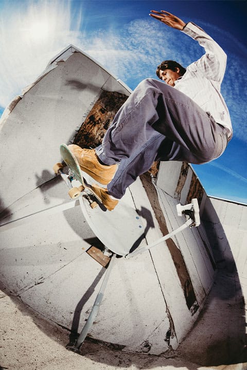 Fisheye-Aufnahme von Nick Michel in braunen Vans Z3, wie er mit seinem Skateboard einen Fs Wallride an einer Betonwand mit Metallkonstruktion ausf&uuml;hrt.