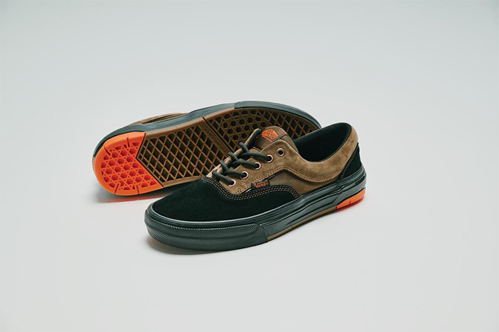 Un paio di Vans Skate Era Vulc nero-marroni con lacci neri, con una scarpa che mostra la suola esterna a nido d&rsquo;ape arancione.