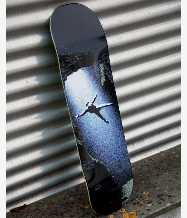 Marketing image of GX1000 Willow Sky Dive 8.25" skateboard deck in glossy black with central light-blue to white sprayed vignette showing a stark black diving silhouette; deck leans against corrugated metal backdrop.